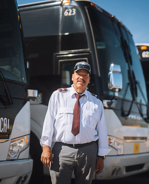 Bus driver in uniform with cap and tie standing in front of a large black coach bus numbered 623.