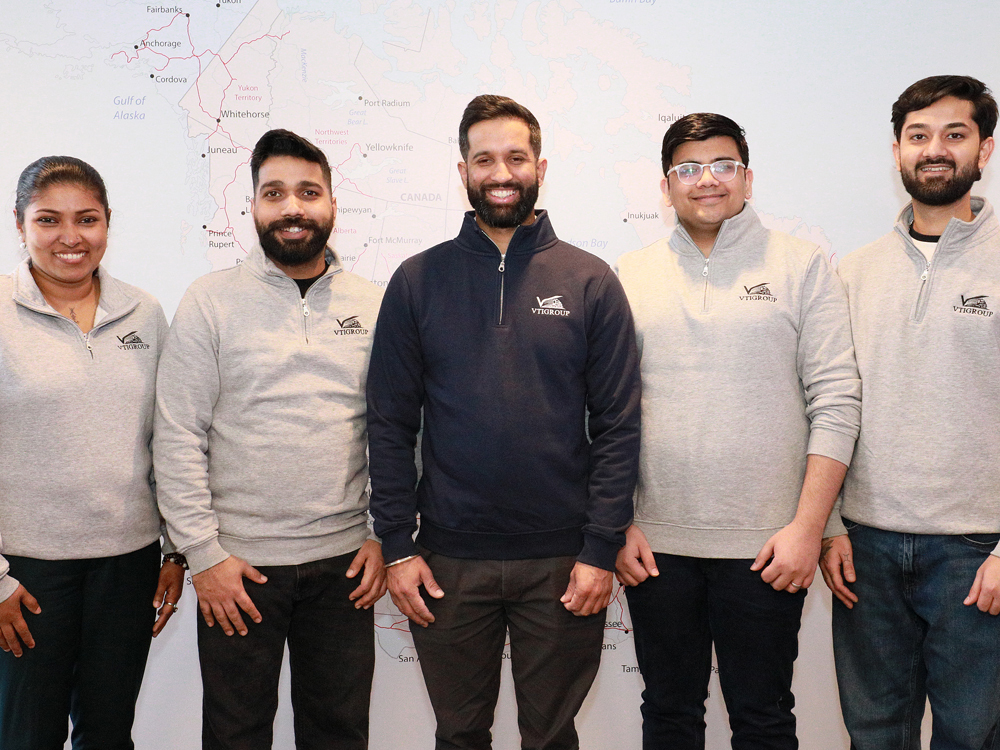 Five team members wearing matching quarter-zip pullovers with company logo standing in front of a map of Alaska.