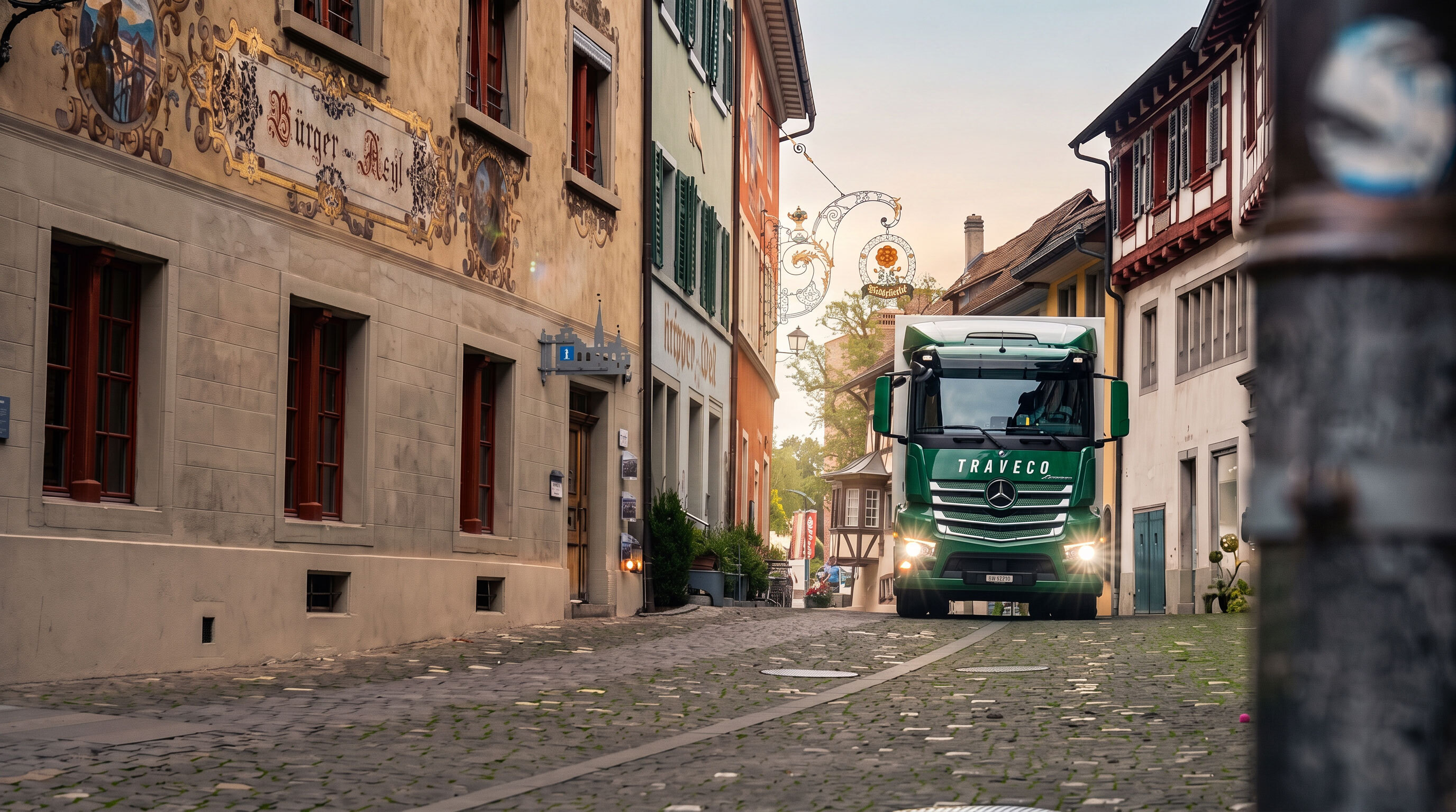 Grüner Mercedes-Benz LKW von Traveco fährt durch eine enge, historische Kopfsteinpflaster-Gasse einer Altstadt.
