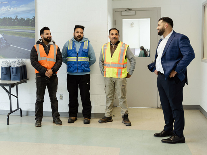 Group of drivers in reflective vests standing next to logistics owner in blue suit.