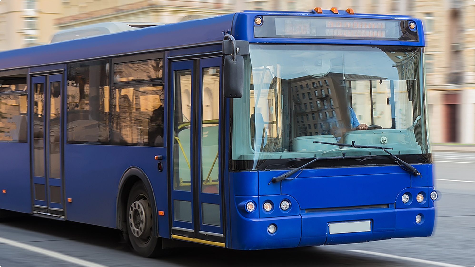 Blauer Stadtbus fährt durch eine verschwommene Stadtkulisse mit Fahrer am Steuer und digitaler Anzeigetafel.