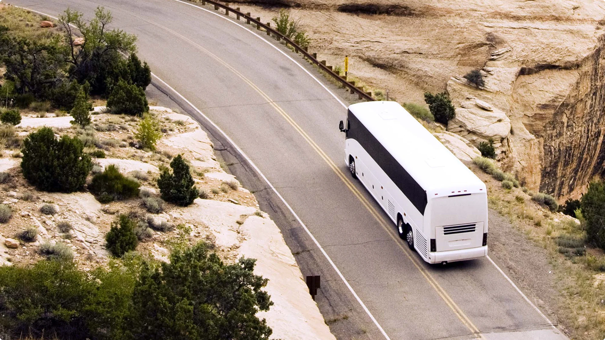 Autocar blanc voyageant sur une route sinueuse à travers un paysage désertique rocheux aux falaises sablonneuses.