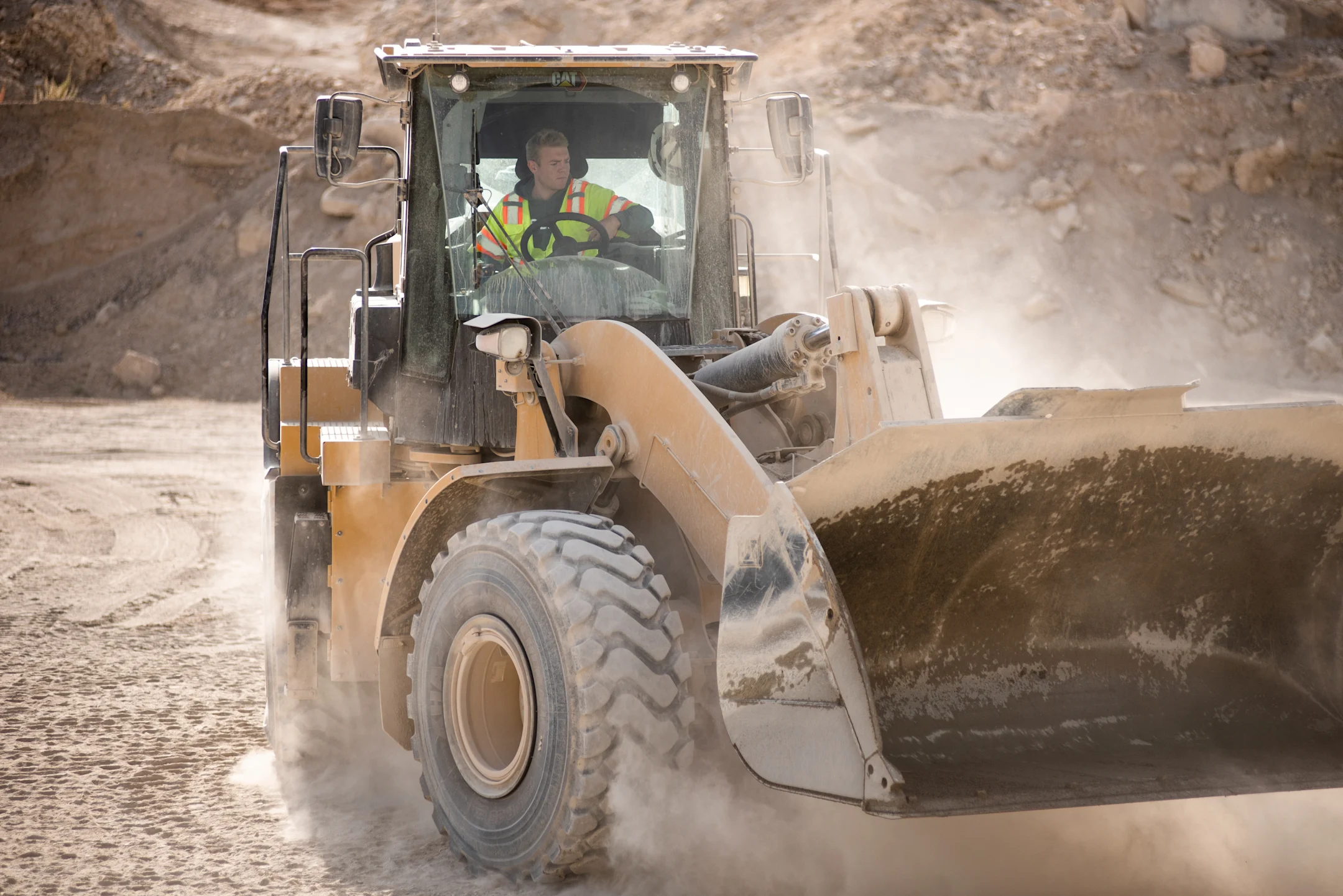 CAT front loader operating at a dusty construction site, operator wearing safety vest visible in cab
