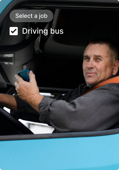 Bus driver in cab of blue bus with "Select a job" interface showing "Driving bus" option checked.