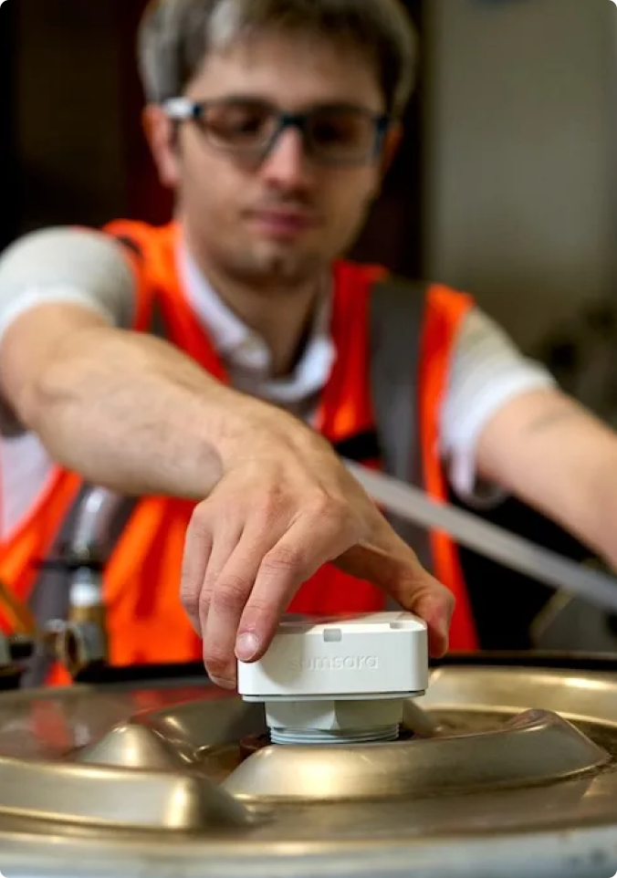 Travailleur en gilet de sécurité orange installant ou réglant un capteur Vaisala blanc sur un équipement industriel.
