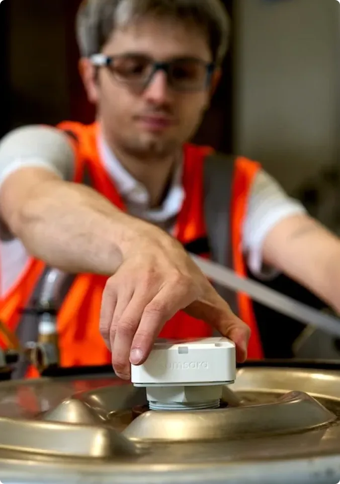 Travailleur en gilet de sécurité orange installant ou réglant un capteur Vaisala blanc sur un équipement industriel.