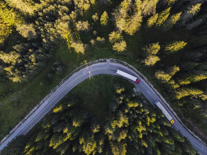 Vista aérea de una carretera con curvas en un denso bosque con tres vehículos.
