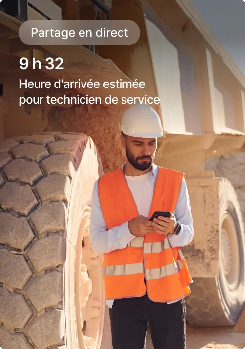 Ouvrier de la construction en gilet de sécurité orange vérifiant son téléphone à côté d'un grand équipement, avec l'affichag