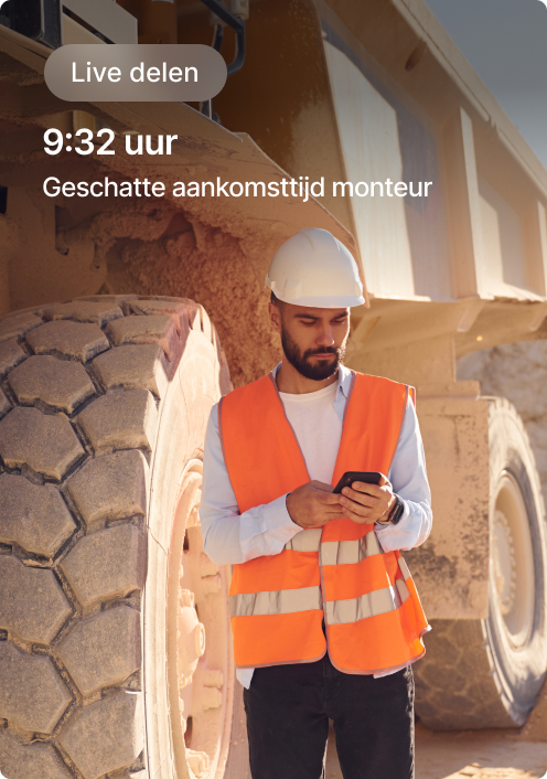 Bouwvakker in oranje veiligheidshesje controleert telefoon naast groot materieel, met scherm geschatte aankomsttijd monteur.