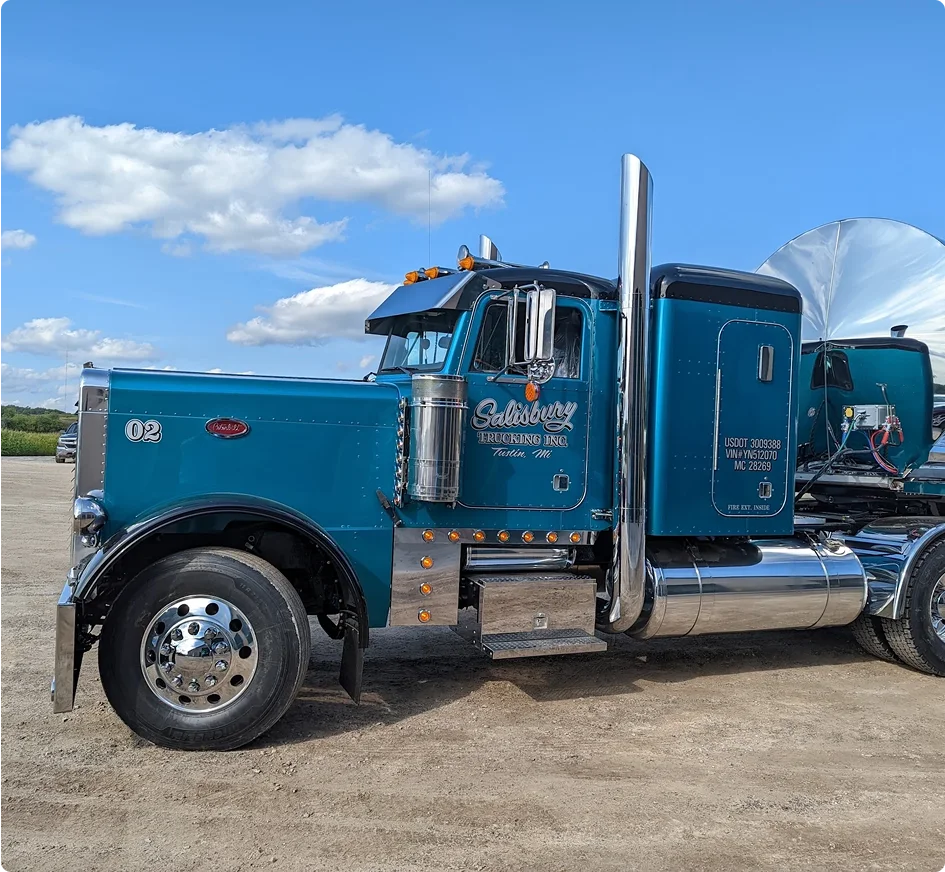 Teal Peterbilt semi truck with chrome exhaust stacks from Salisbury Trucking parked under blue sky with white clouds.