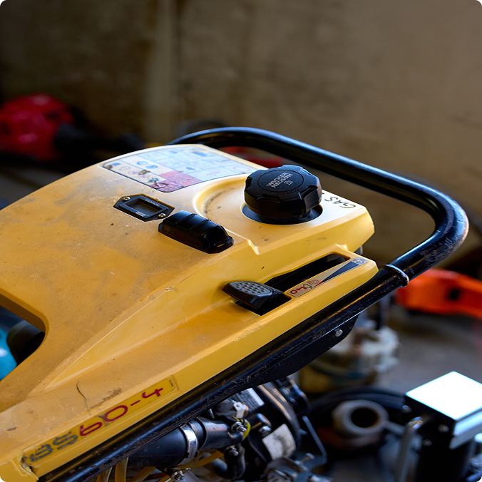 Close-up of yellow construction equipment control panel with black fuel cap and switches on metal frame.