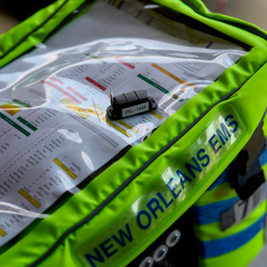 A bright green New Orleans EMS bag with a clear pocket holding medical reference charts and a labeled lock.