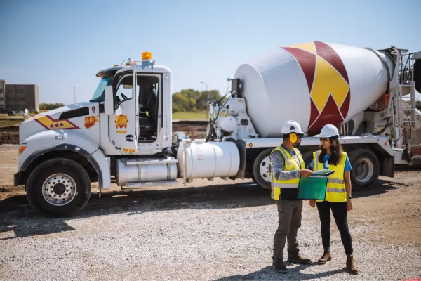 Two people standing in front of a Rasmussen Group cement mixer.