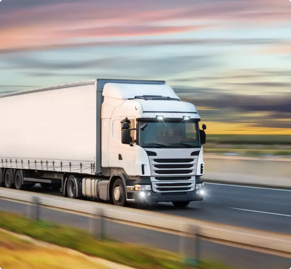 Blue semi-truck with silver trailer driving on highway with evergreen forest backdrop