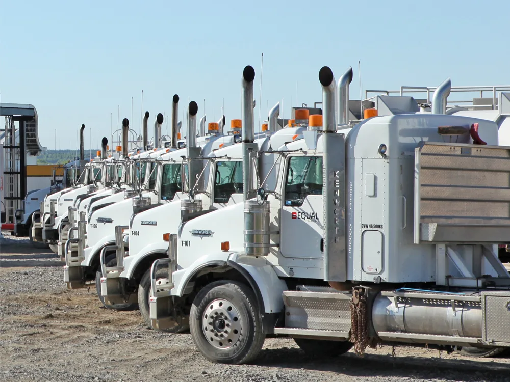 Row of white oil and gas transportation trucks in yard.
