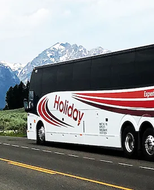 White and red Holiday tour bus driving on a highway with snow-capped mountains in the background.