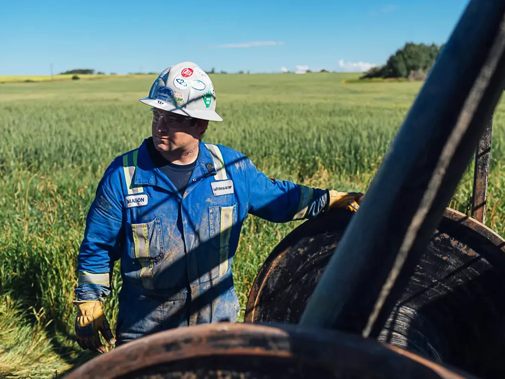 Worker in blue uniform and hard hat standing in grassy field next to Whitewater Management LP equipment