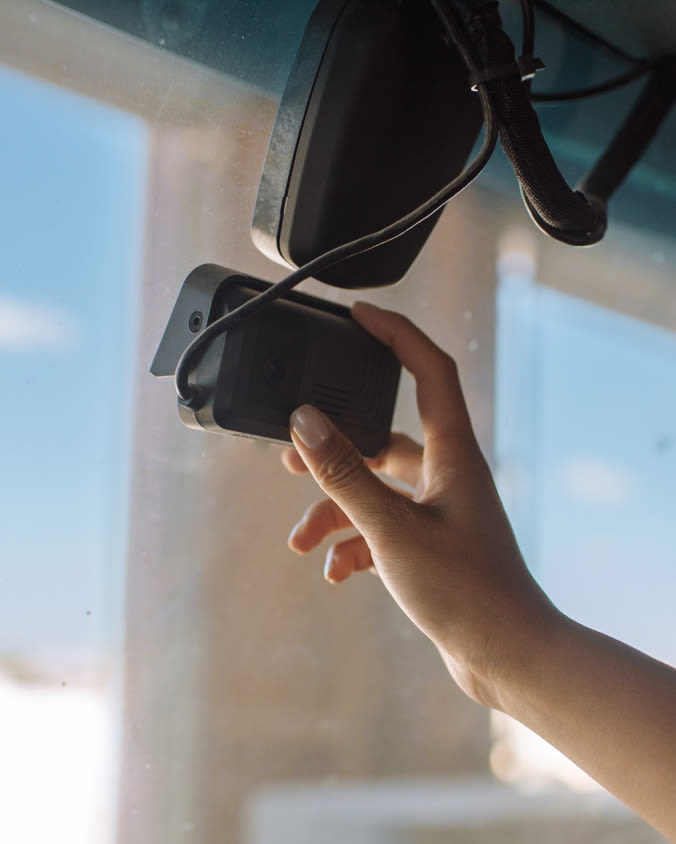 A hand adjusting a Samsara dash cam that's installed on a windshield inside of a truck.