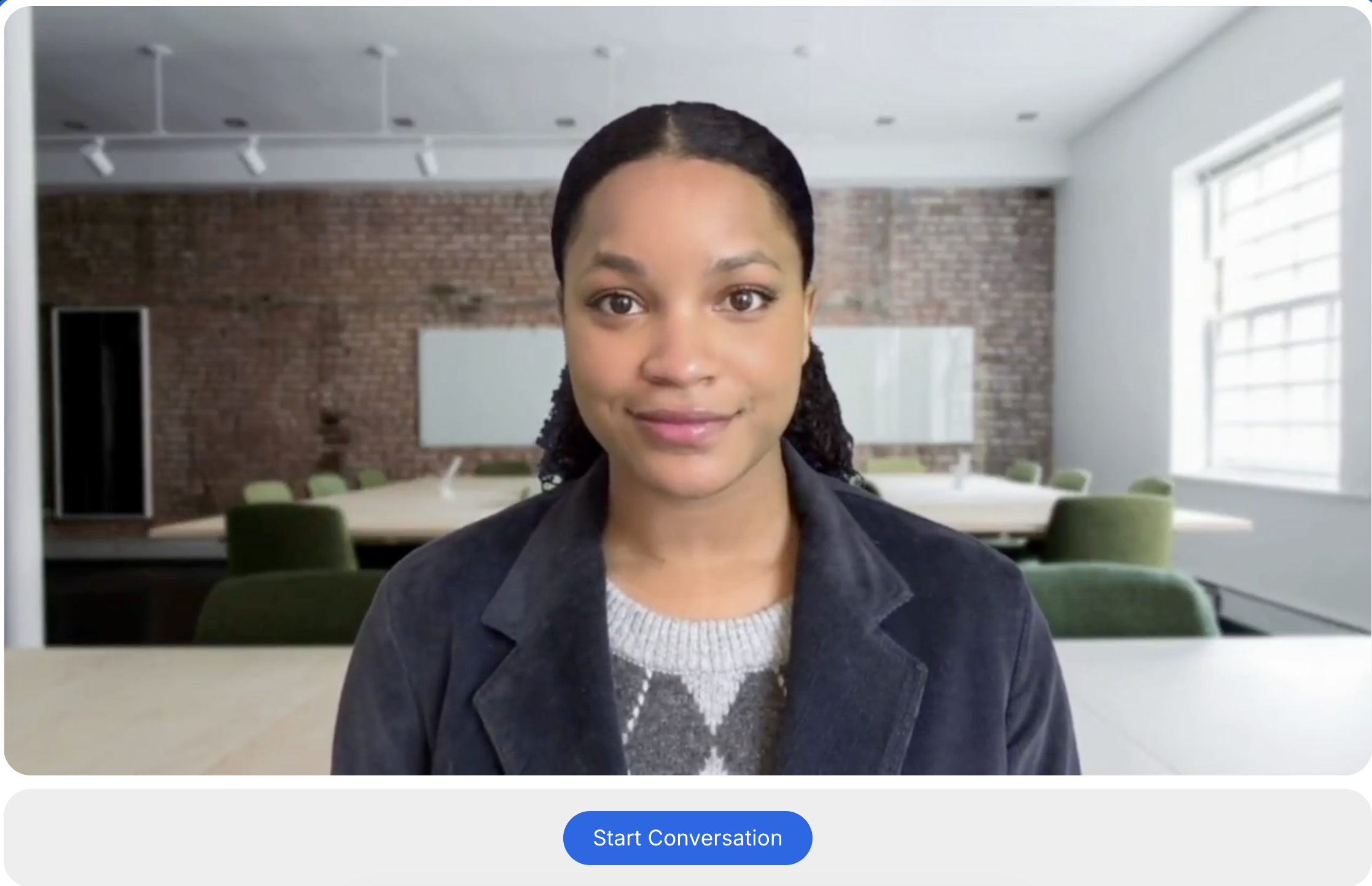Person in dark blazer and gray sweater in modern conference room with exposed brick wall and green chairs.