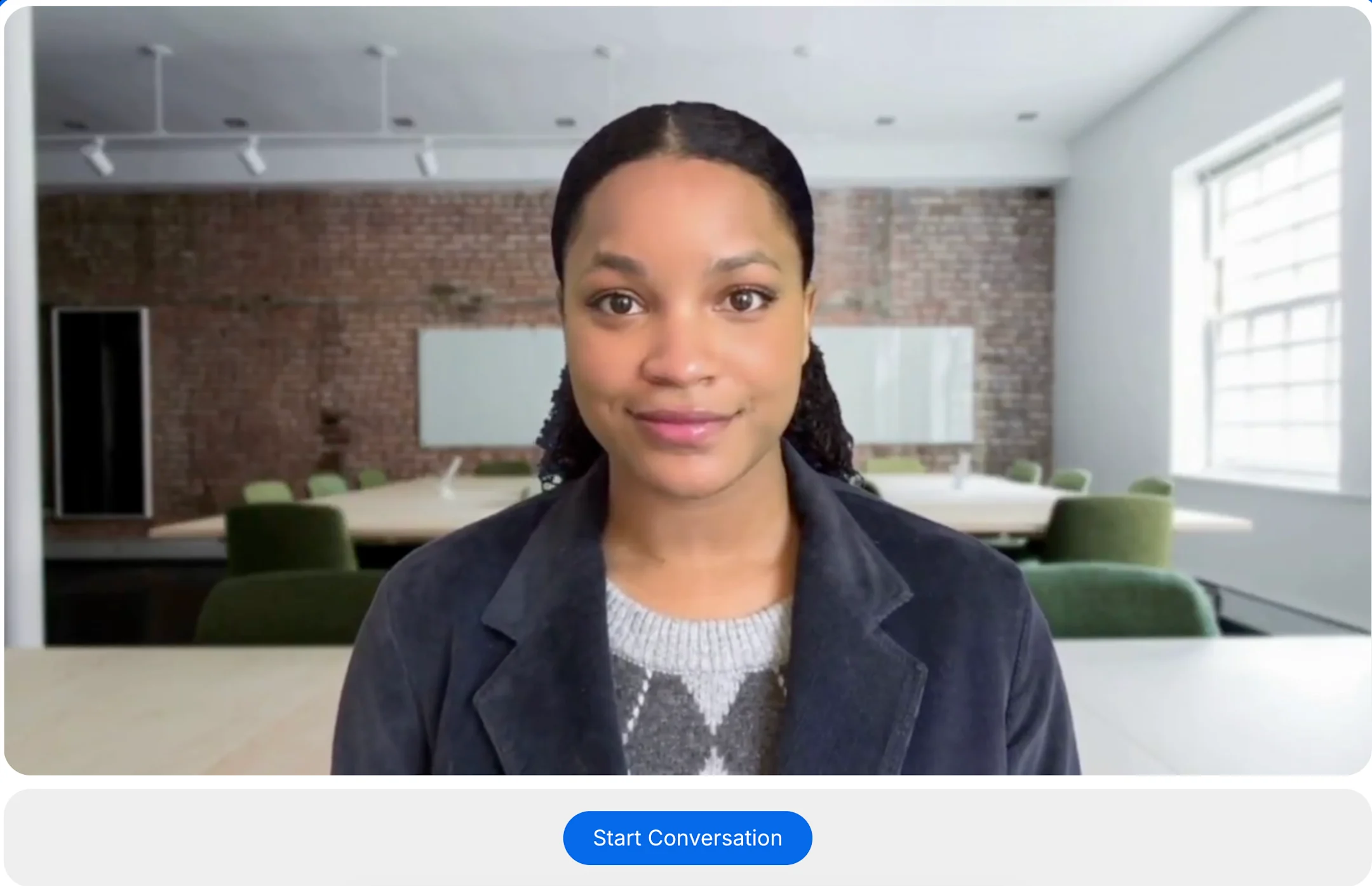 Person in dark blazer and gray sweater in modern conference room with exposed brick wall and green chairs.
