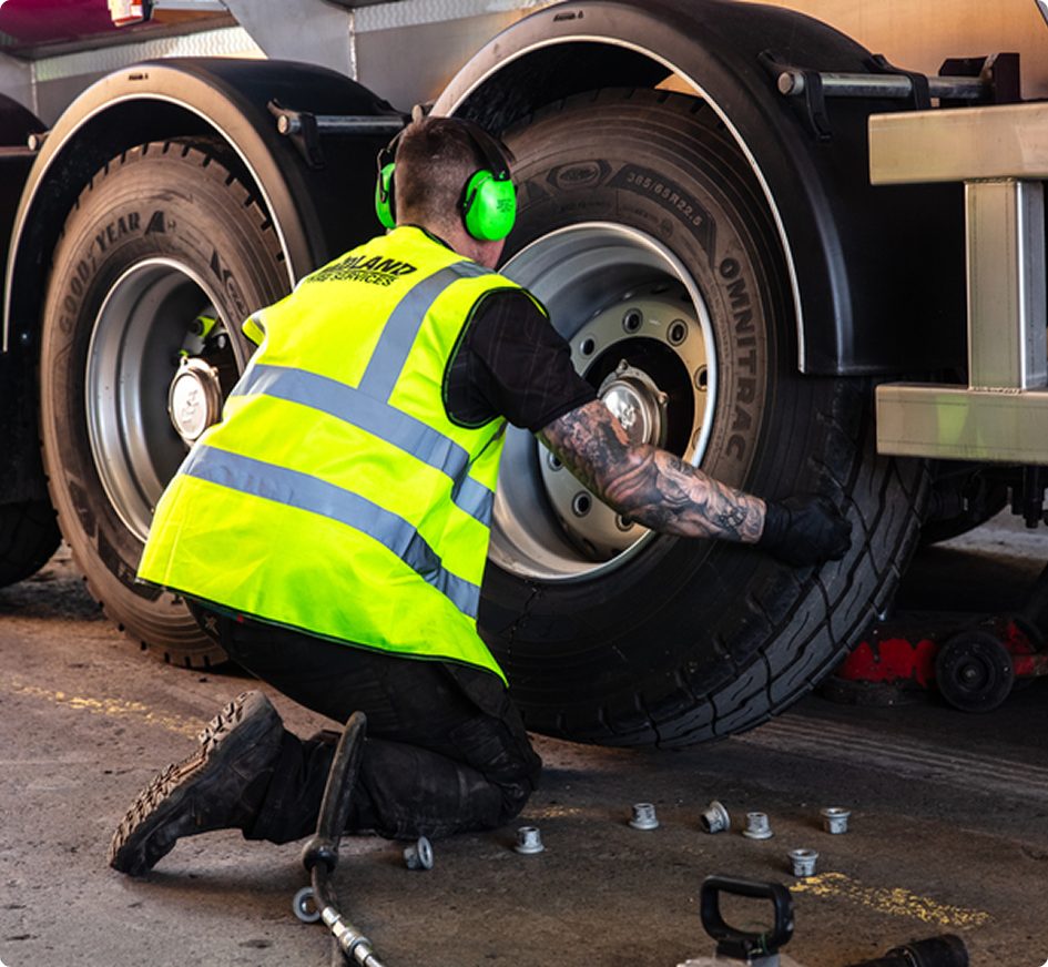 Werknemer in blauw uniform met neongroene handschoenen die machines bedient in een zwak verlichte loods.