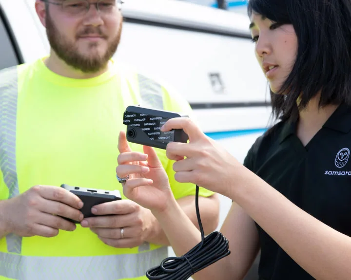 A woman holding a dash cam is showing a man in a yellow reflective vest features on the product.