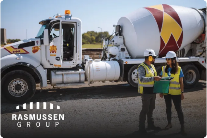 Grupo Rasmussen, dos trabajadores de pie junto a un camión grande con equipo de protección personal