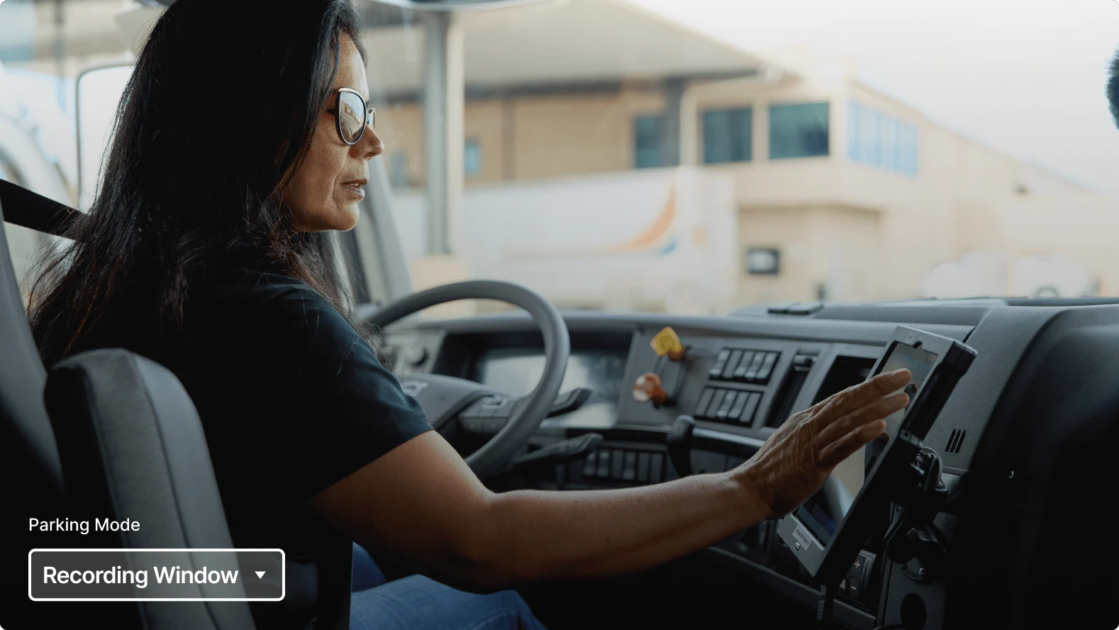 Person with long dark hair wearing glasses operating a dashboard touchscreen in a commercial vehicle.