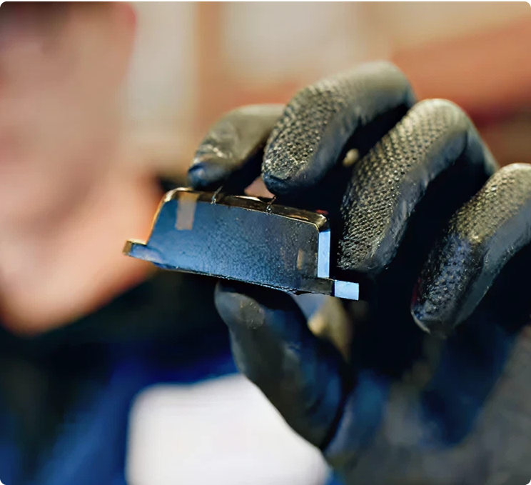 Hand in black protective glove holding a small electronic component or circuit board with blue elements.