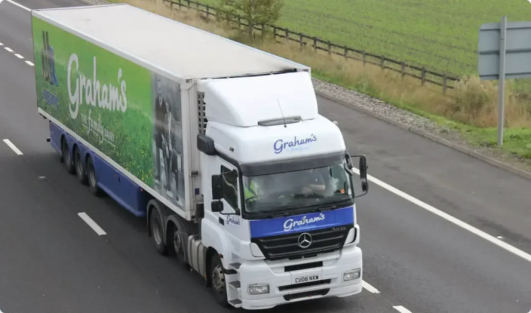 White and blue Graham's dairy delivery truck with green branding driving on a motorway beside green fields.