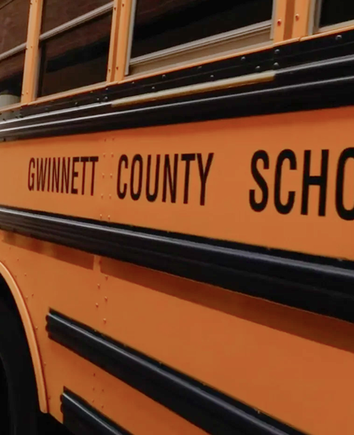 Close-up of an orange Gwinnett County school bus showing partial text and windows with black trim.