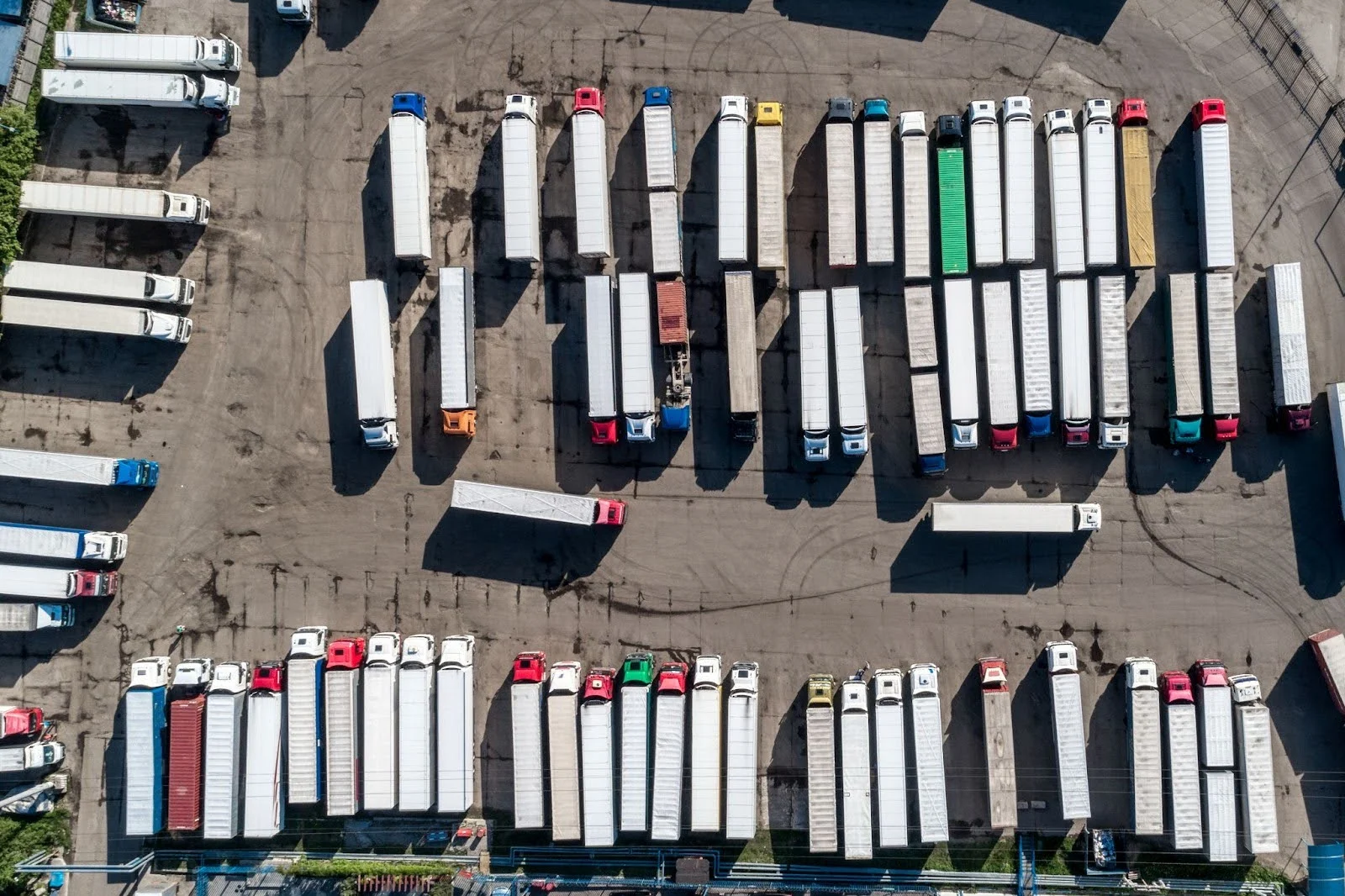 Aerial view of a lorry depot with rows of articulated trucks parked in formation, featuring colourful cab units and white trailers.
