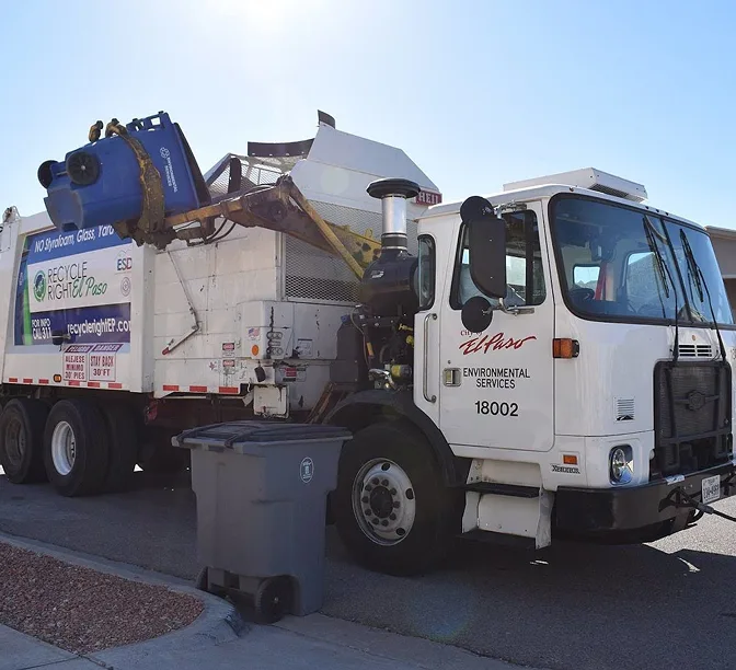 White El Paso Environmental Services garbage truck with mechanical arm lifting a trash bin on a suburban street.