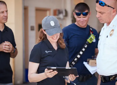 Une femme portant un chapeau tient une tablette tout en souriant; trois hommes sont également sur l’image