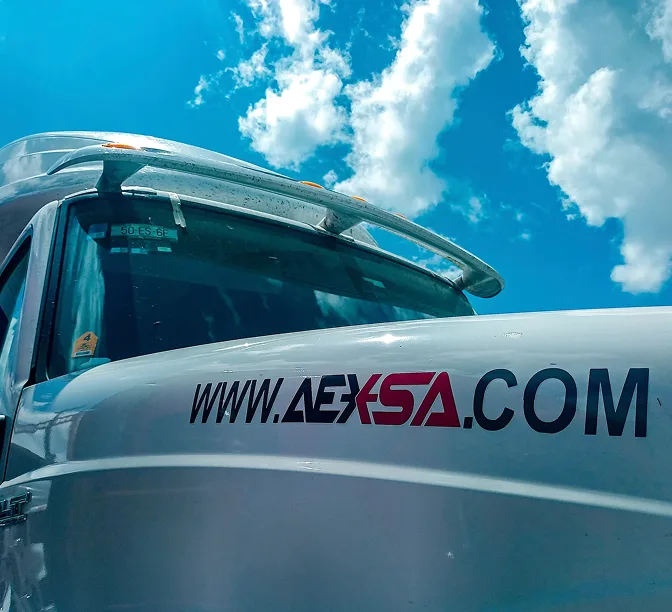 Primer plano de un camión blanco con el sitio web www.AEXSA.com en el costado, bajo un cielo azul con nubes blancas.