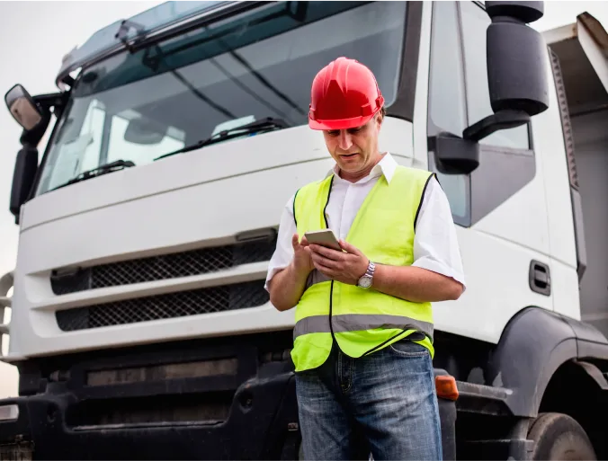 Worker standing in front of a truck holding a phone