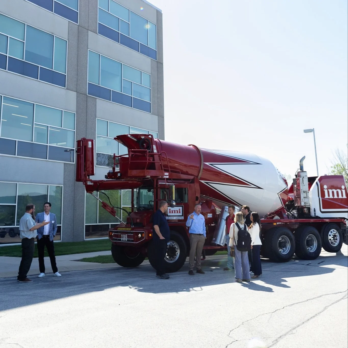 Groupe de personnes discutant près d'un camion malaxeur rouge et blanc IMI devant un immeuble moderne.