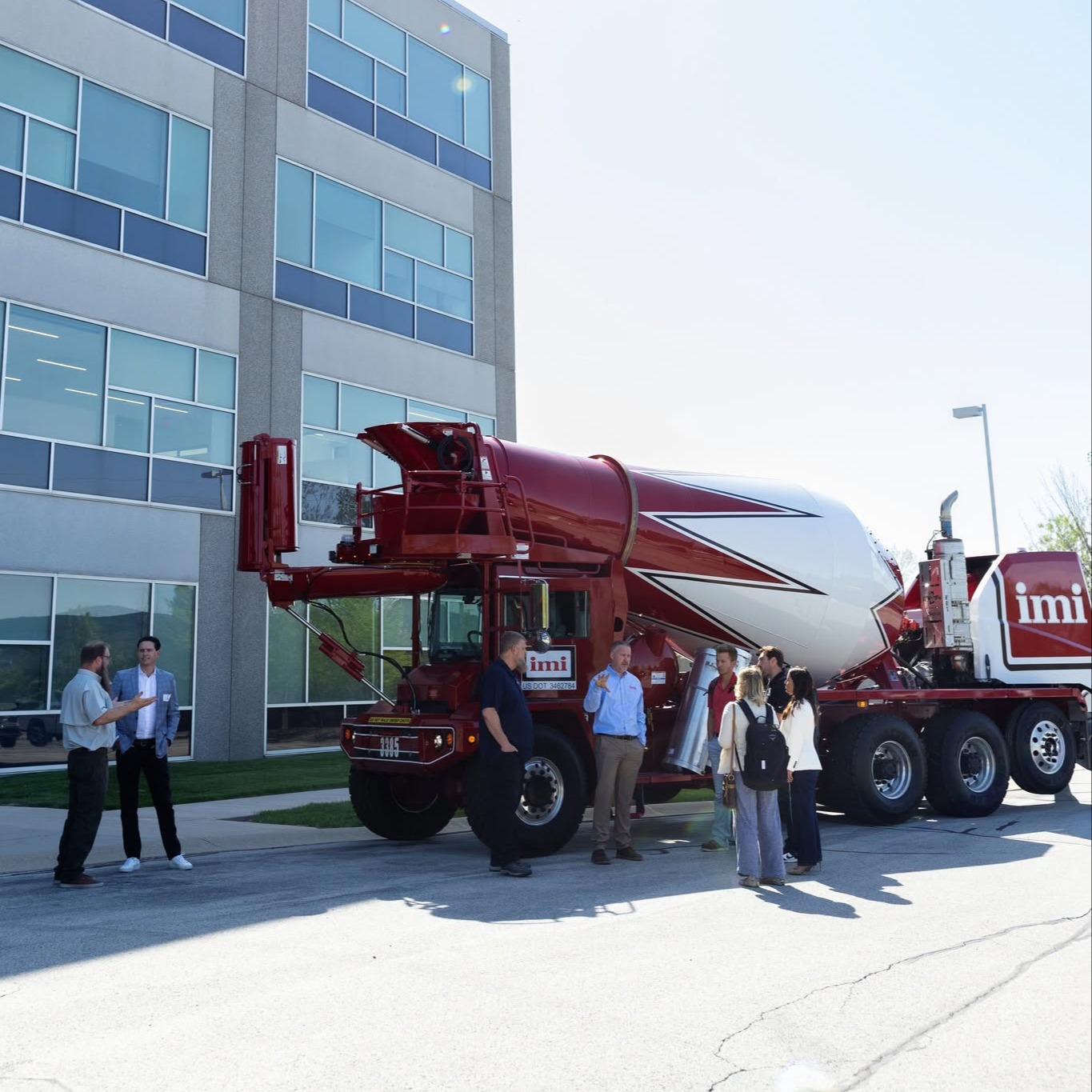 Groupe de personnes discutant près d'un camion malaxeur rouge et blanc IMI devant un immeuble moderne.
