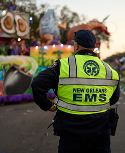 EMS worker in bright yellow vest watching over a colorful Mardi Gras parade float in New Orleans.