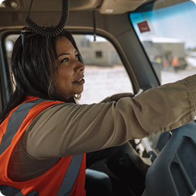Person in orange safety vest driving a vehicle, focused on the road ahead.