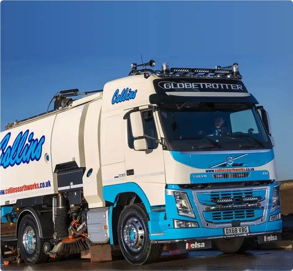 Weißer und blauer Volvo Globetrotter-LKW mit „Collins“-Branding und Kehrmaschinenaufsätzen vor klarem blauen Himmel.