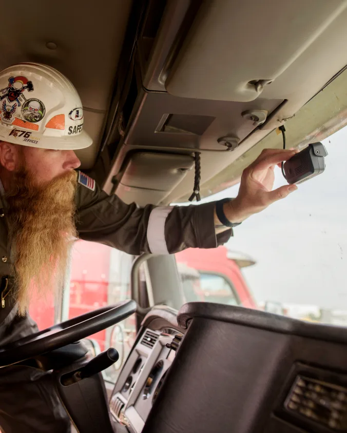 Commercial truck driver with safety hard hat adjusting Samsara dash camera