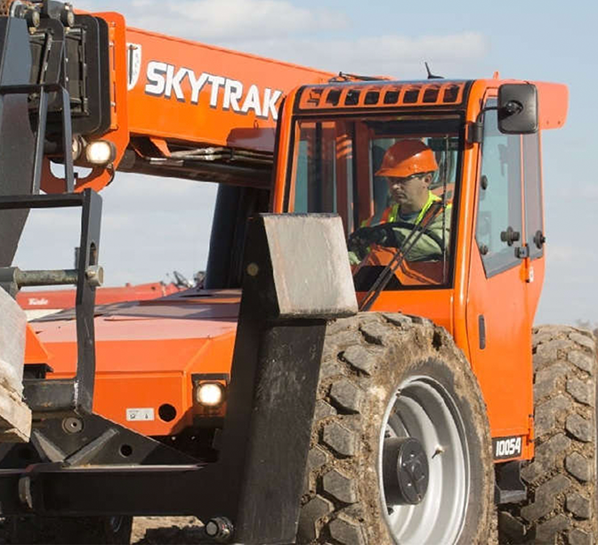Orange SKYTRAK telehandler with operator in safety gear operating the construction equipment on a job site.