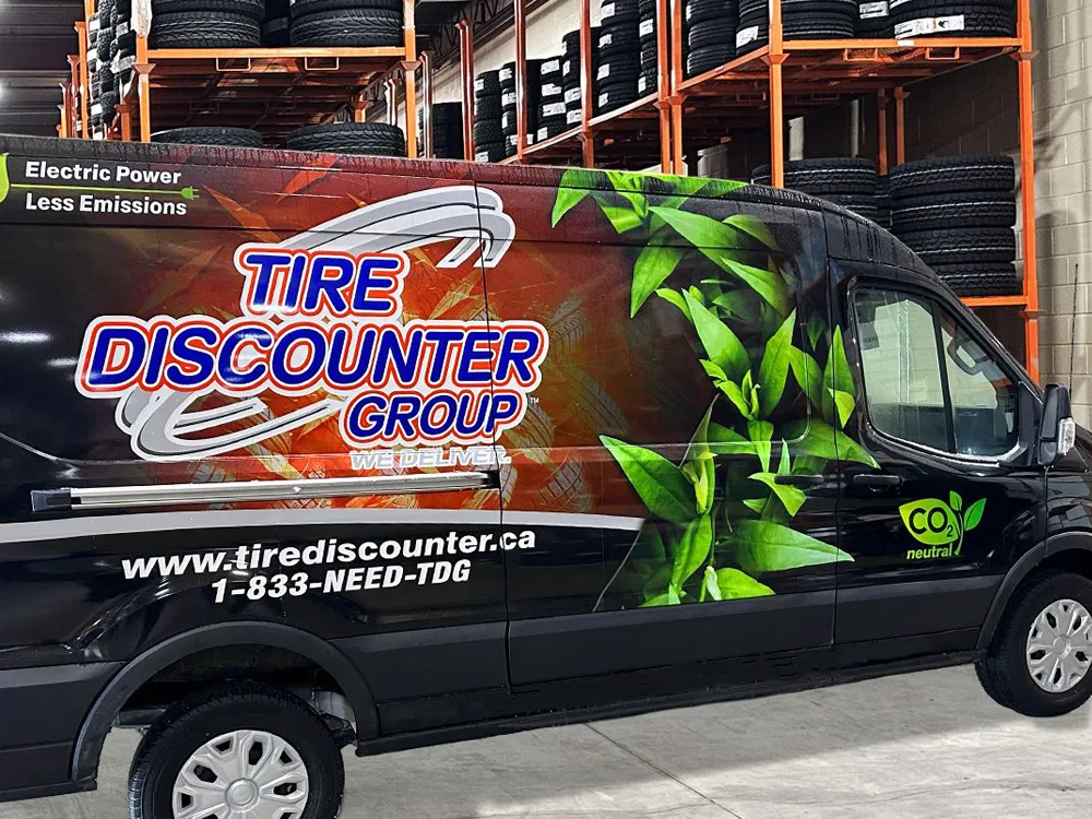 Camion de Tire Discounter Group dans un entrepôt avec des pneus noirs sur des étagères orange en arrière-plan.