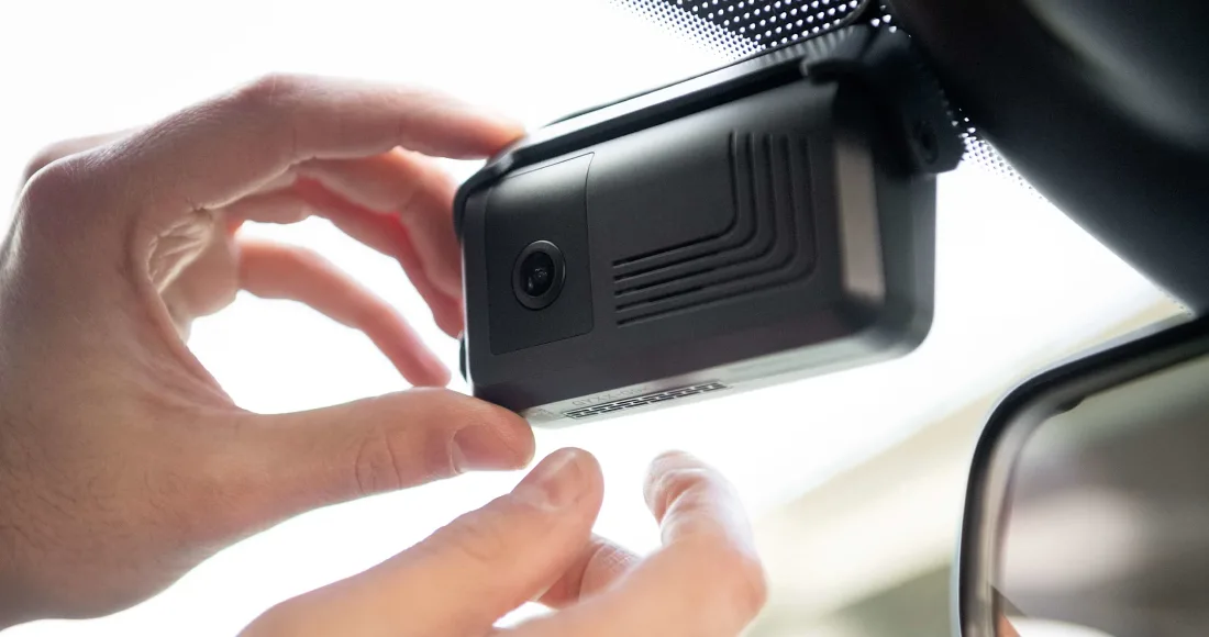 Hand installing or adjusting a black dashboard camera mounted on a car windshield near the rearview mirror.