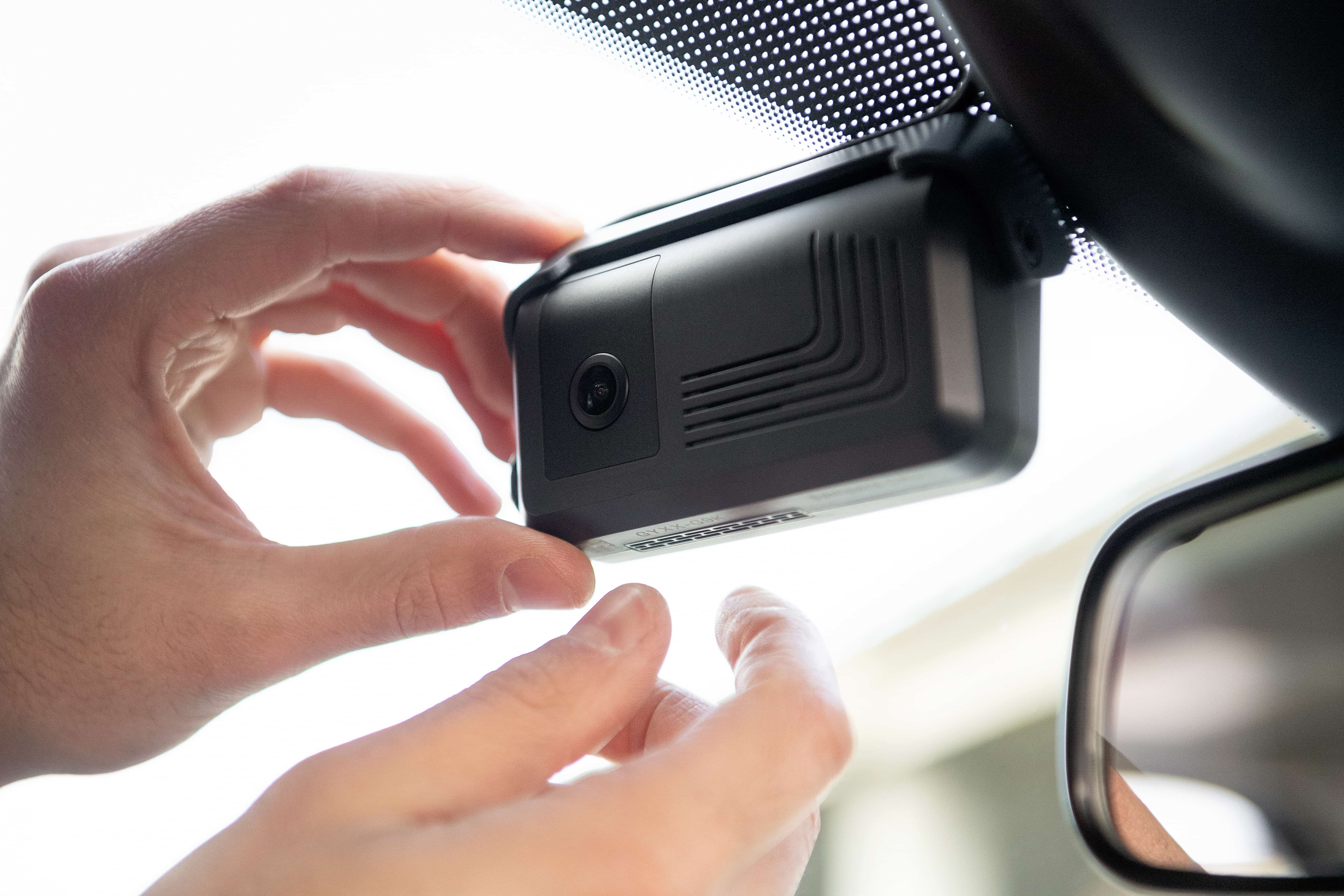 Hand installing or adjusting a black dashboard camera mounted on a car windshield near the rearview mirror.