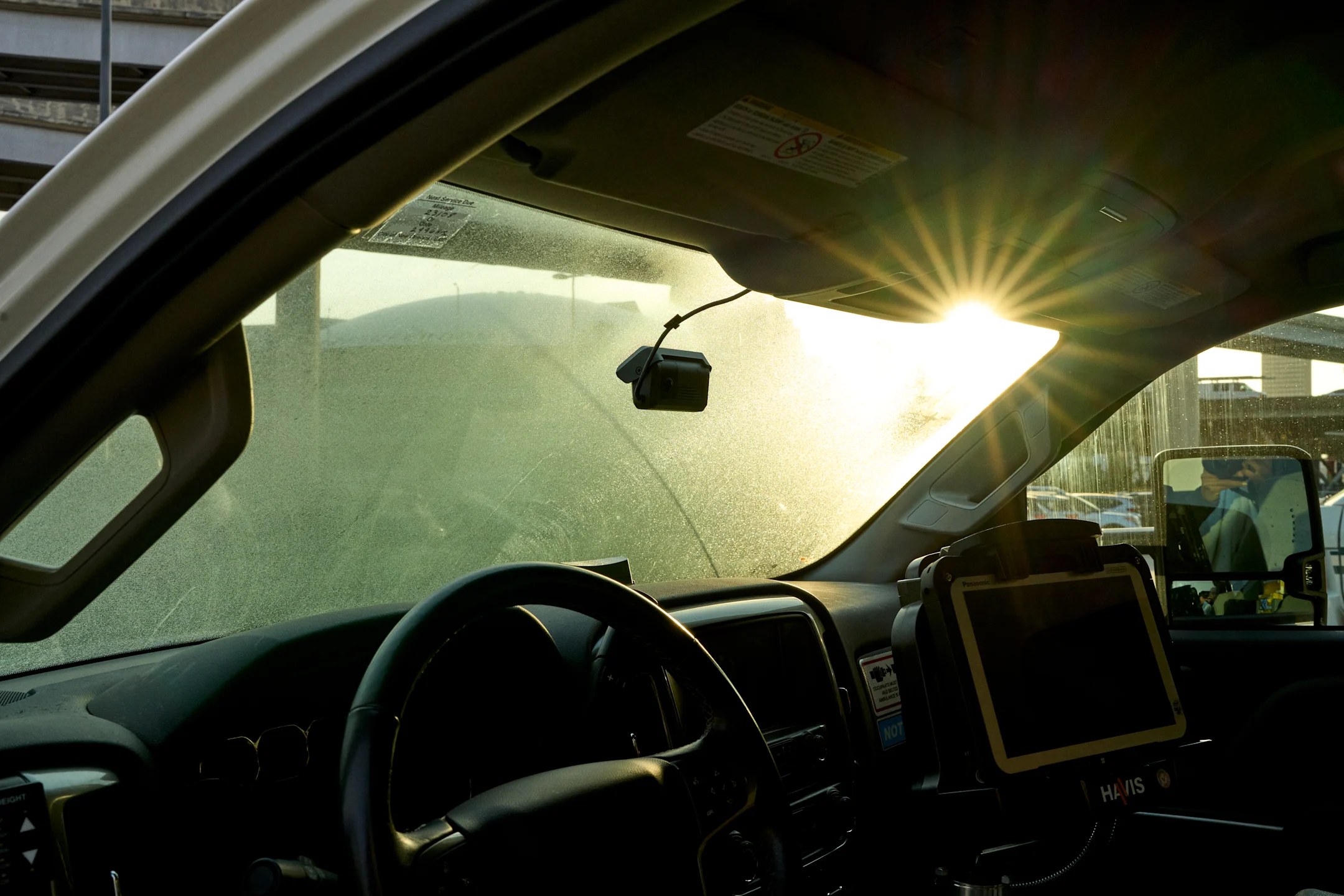 View from inside a vehicle with sunlight streaming through dusty windshield, dashboard with mounted tablet visible.