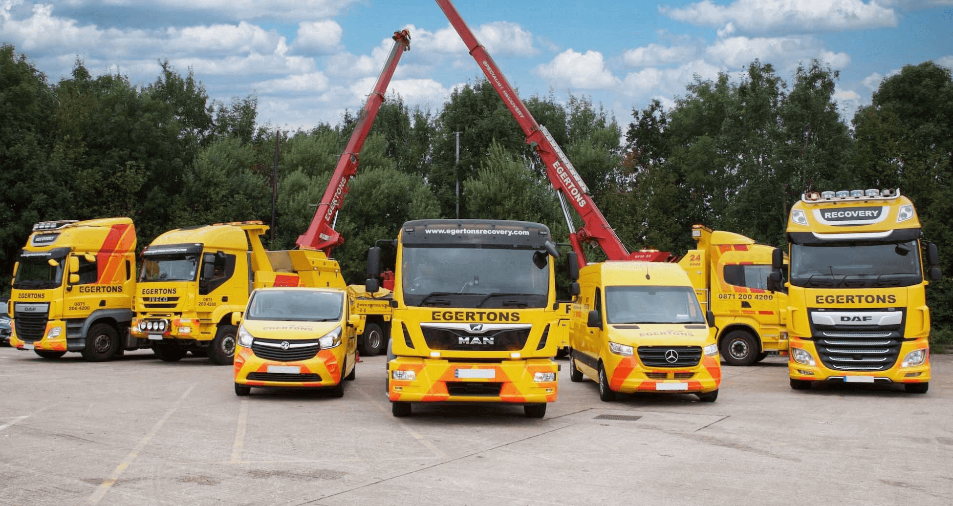 Fleet of yellow Egertons recovery vehicles including trucks, vans and cranes parked in a yard under blue sky.