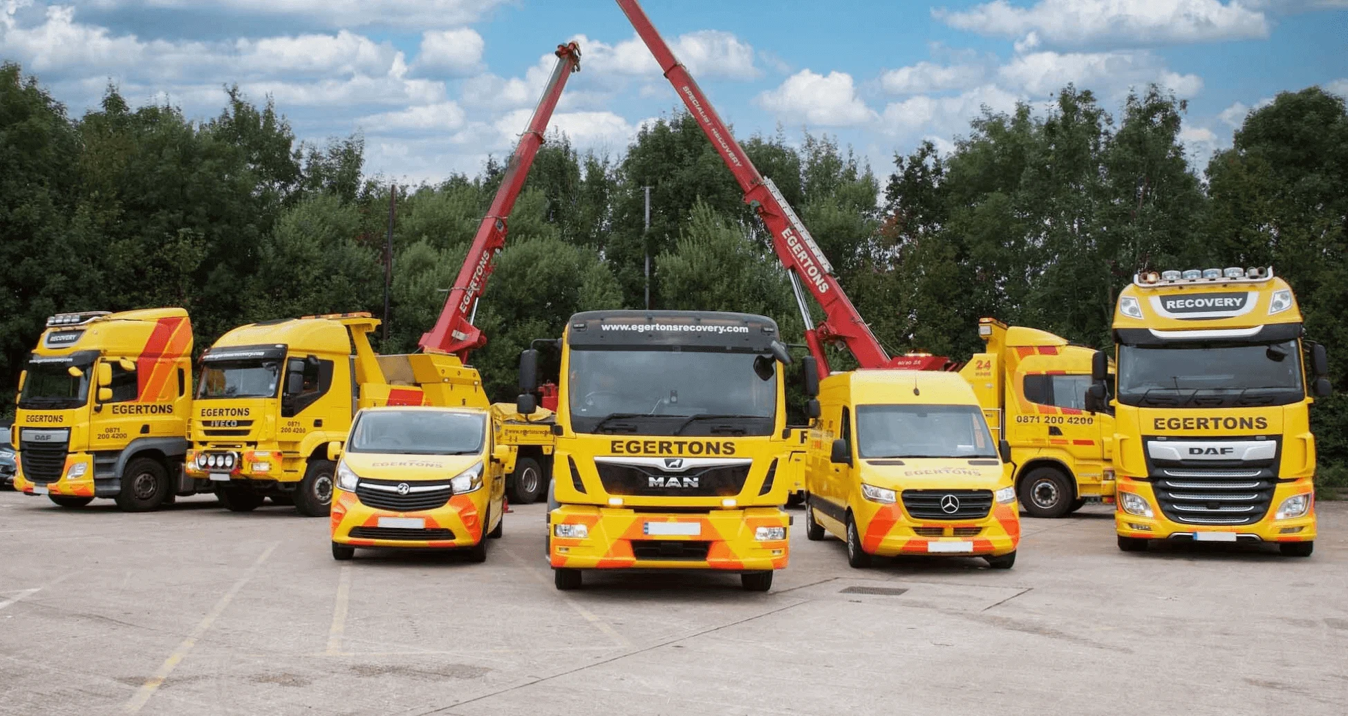 Fleet of yellow Egertons recovery vehicles including trucks, vans and cranes parked in a yard under blue sky.