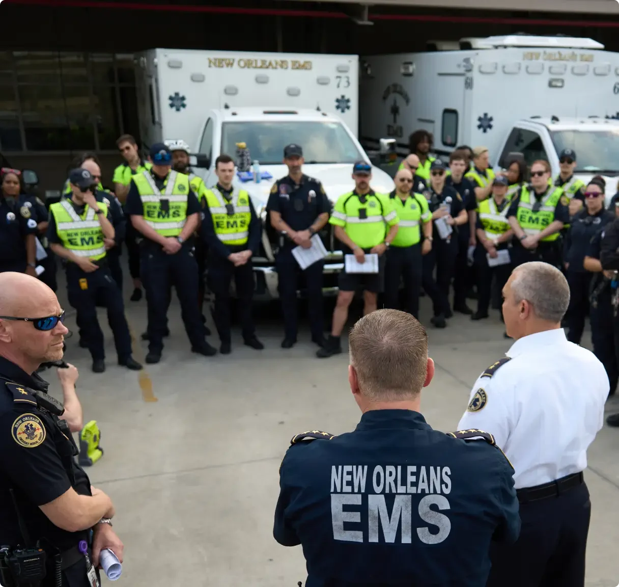New Orleans EMS personnel gathered for briefing in front of ambulances, with officers addressing the group.